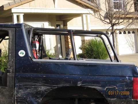 1994 Ford Bronco - Side view of a dark blue SUV an interior roll cage and a mounted fire extinguisher, with a visible date stamp.