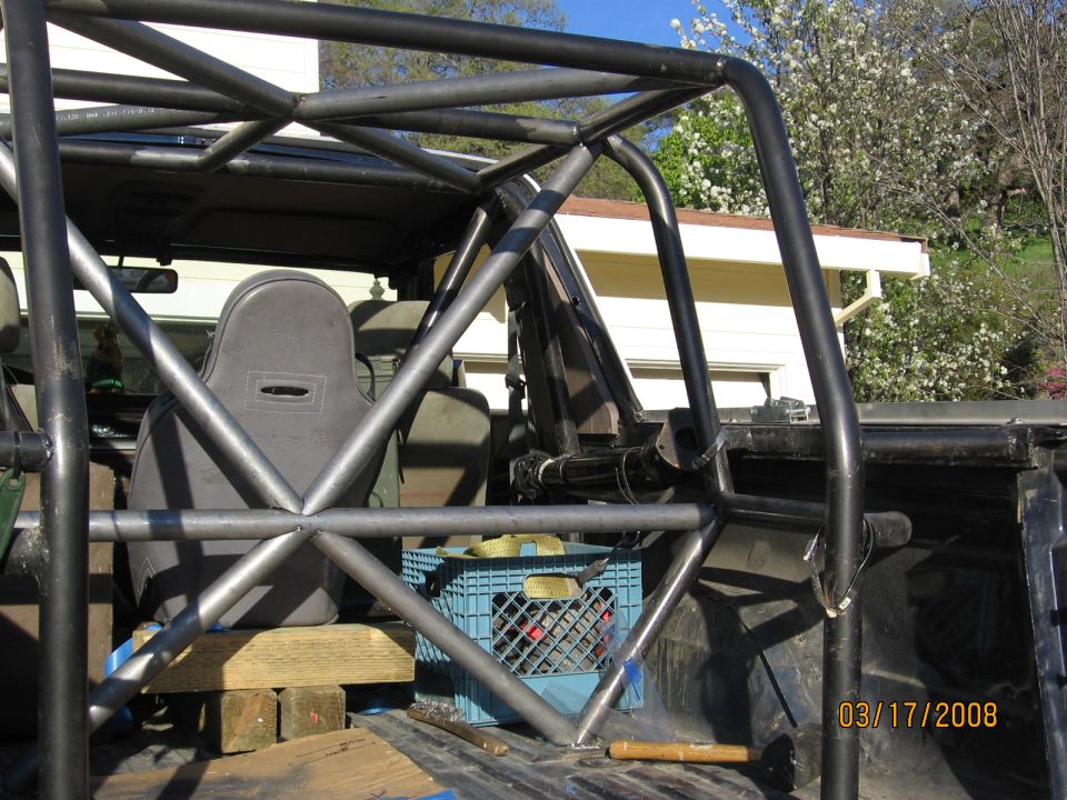 Roll cage tubing inside a truck bed, with a blue milk crate and wooden blocks