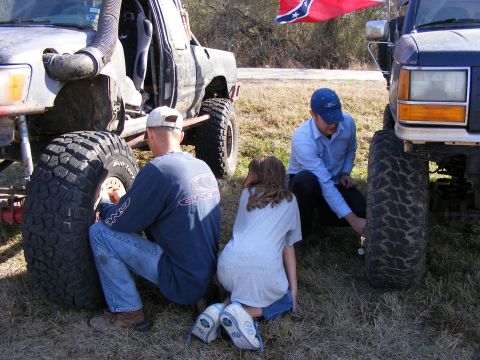 1981 Jeep CJ7 - People attend to tires on heavily modified off-road vehicles under a Confederate flag.