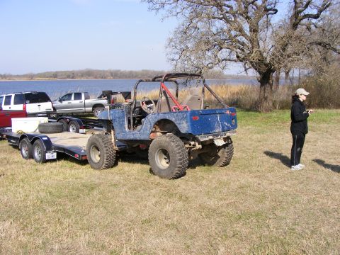 1981 Jeep CJ7 - A blue Jeep is parked on a grassy area near a lake, with a trailer and other vehicles in the background.