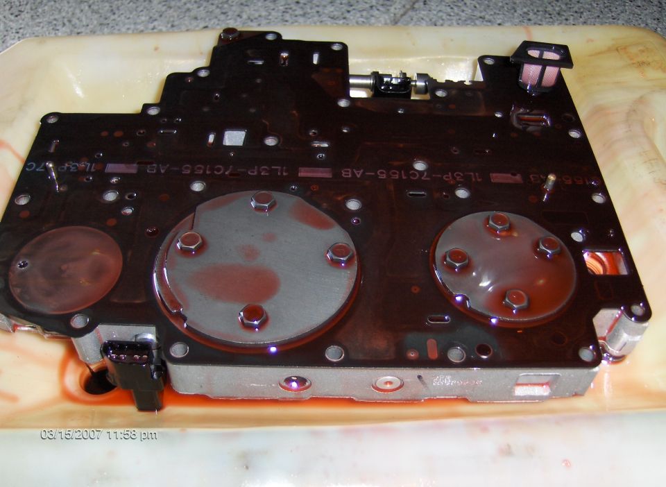 Valve body covered in red transmission fluid, with visible metal components and circuit board