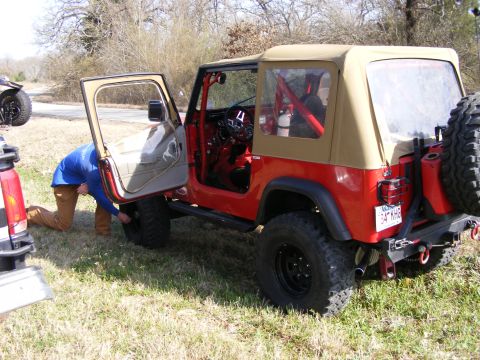 1981 Jeep CJ7 - A red 1981 Jeep CJ7 with a tan soft top is shown with its driver's door open as a person works on the front tire. Another vehicle is partia…