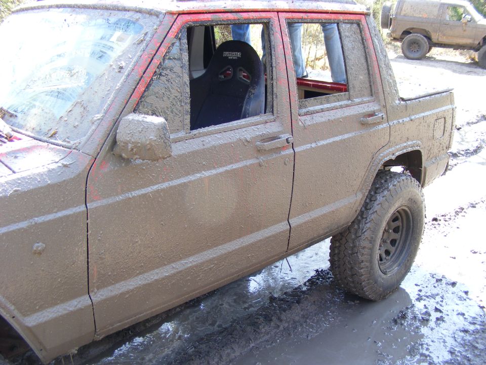 Mud-covered red Jeep Cherokee XJ side view with racing seat visible