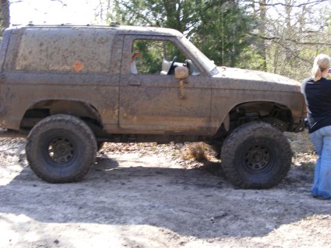 1981 Jeep CJ7 - A heavily muddied 1983 Ford Bronco II sits off-road, modified with a lift kit and oversized tires.