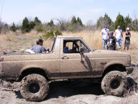 1981 Jeep CJ7 - Muddy 1987 Ford Bronco navigates rough terrain with onlookers present.