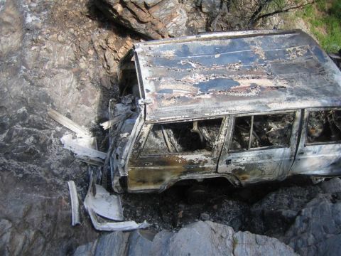 1987 Suzuki Samurai - Wreckage of a heavily damaged SUV is visible on a rocky incline, showing extensive fire damage.