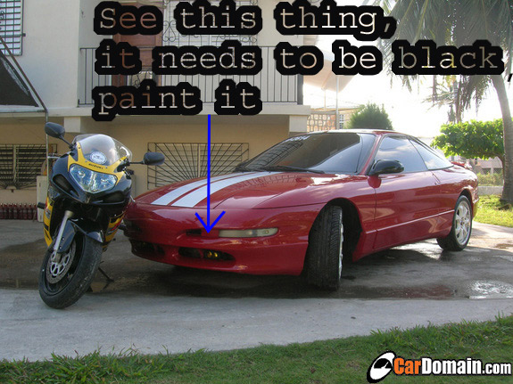 Red 1993 Ford Probe coupe with white racing stripes on the hood, parked next to a yellow and black motorcycle