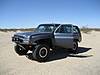 1986 Ford Bronco - A gray SUV sits in a sandy, desert landscape with its doors open under a clear blue sky.