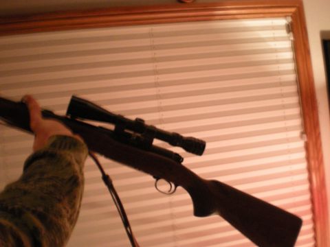 1993 Ford Bronco - A rifle with a scope is held by a person in front of a window blind.