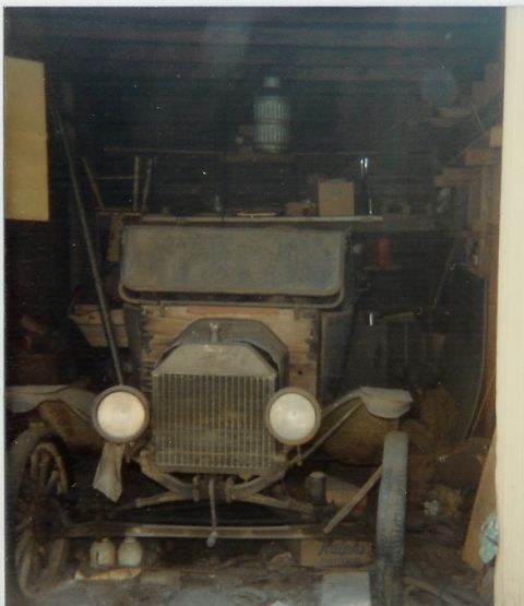 1973 Ford Ranchero - A vintage car, possibly a Model T, sits in a cluttered garage, its front end visible.