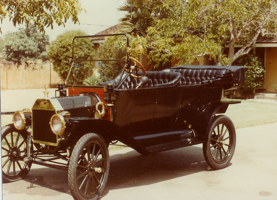 Black touring car with a black top and tufted seats, brass headlights, and wooden steering wheel
