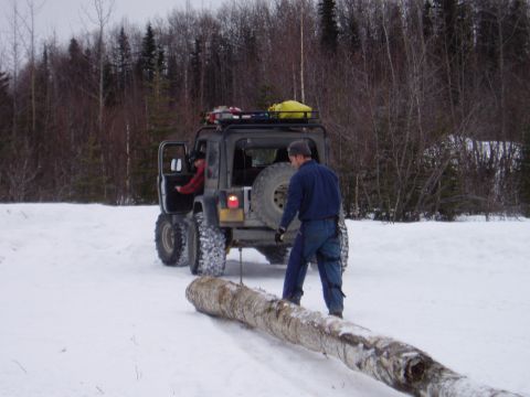 2000 Ford E350 - A Jeep Wrangler is used to drag a large log through a snowy forest scene.