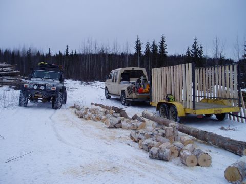 2000 Ford E350 - Two vehicles and a trailer are parked in a snowy logging area with cut logs scattered around.