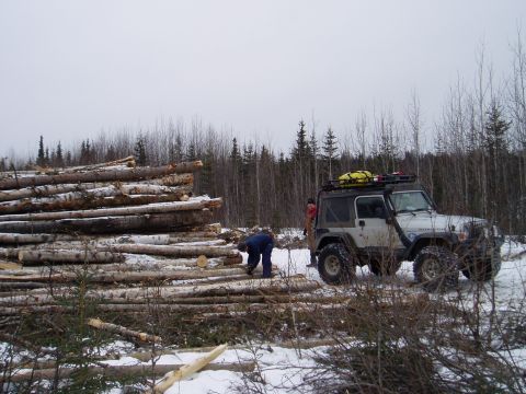 2000 Ford E350 - A person works near a stack of logs while a modified Jeep Wrangler sits nearby in a winter forest setting.