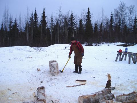 2000 Ford E350 - A man prepares to chop wood in a snow-covered area, with a line of trees behind him.