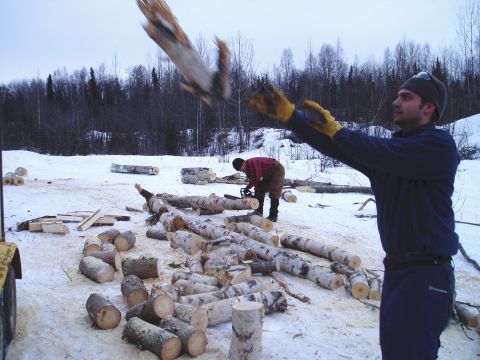 2000 Ford E350 - Two men are working in a snowy area, cutting and moving logs, with a yellow vehicle part visible on the left.