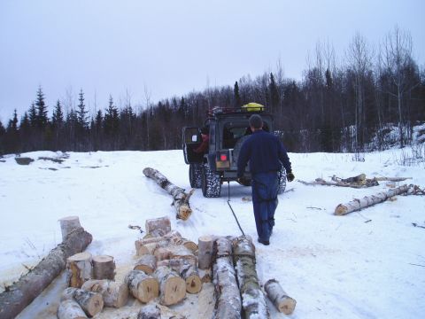 2000 Ford E350 - A Jeep Wrangler is used to drag logs through a snow-covered area, with a person walking behind it.