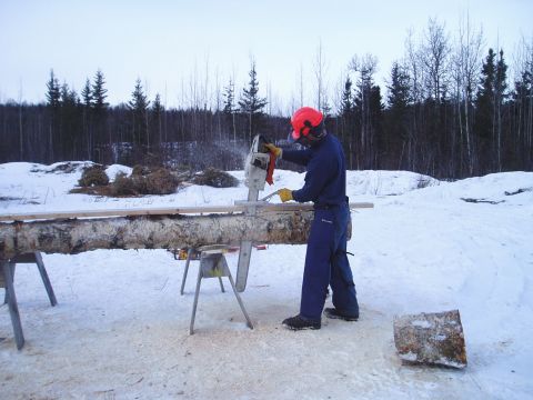 2000 Ford E350 - A person operates a chainsaw to cut a log supported by sawhorses in a winter landscape.