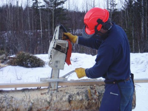 2000 Ford E350 - A person uses a chainsaw mill attachment to cut a log in a snowy environment.