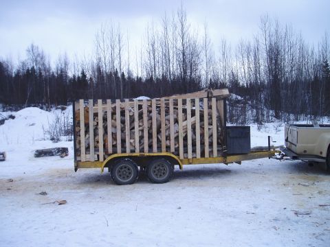 2000 Ford E350 - A pickup truck is hitched to a trailer filled with cut firewood, set against a backdrop of trees and snow.