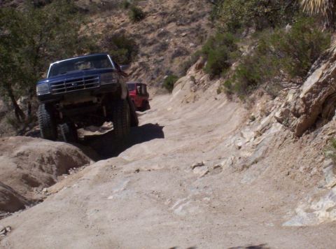 1992 Ford F-150 - Two trucks navigate a challenging off-road path in a rocky, arid landscape.