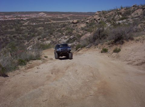 1992 Ford F-150 - A lifted 1992 Ford F-150 navigates a dusty, off-road trail with a vast, hilly terrain in the background.
