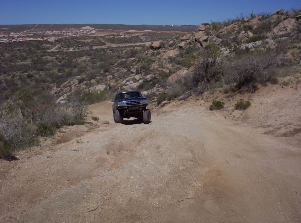 1992 Ford F-150 driving up a dirt road in a rocky, arid landscape