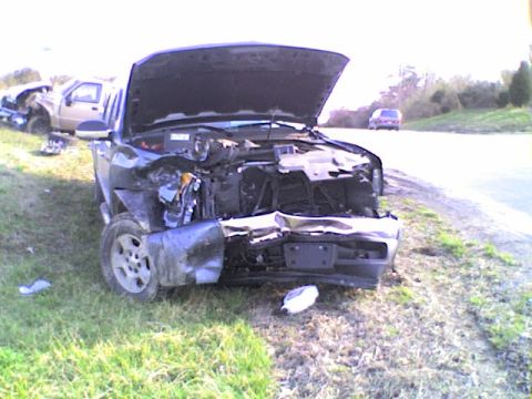 1990 Ford Bronco - Two wrecked pickup trucks sit on the side of the road after an accident.