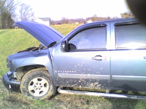 1990 Ford Bronco - A silver pickup truck sits in a grassy field with its hood open and mud splattered on its side.