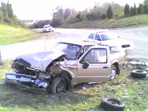 1990 Ford Bronco - A severely damaged pickup truck sits on the roadside with two police cars present at the scene.