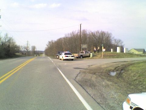 1990 Ford Bronco - Two vehicles, a police car and a pickup truck, are stopped on the side of a road with people nearby.