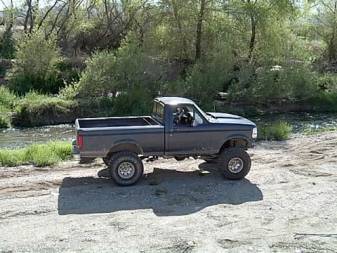 1992 Ford F-150 - This lifted 1992 Ford F-150 pickup truck is seen parked off-road near a body of water.