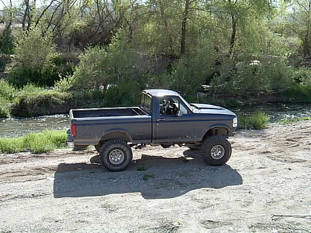 Dark blue 1992 Ford F-150 pickup truck with large tires parked by a river