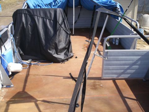 Pontoon boat deck with a black cover over an object, blue tarps, and metal railings