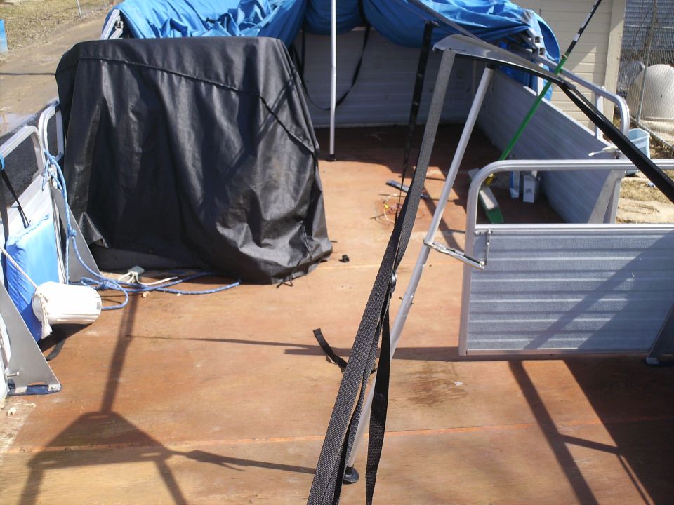 Pontoon boat deck with a black cover over an object, blue tarps, and metal railings
