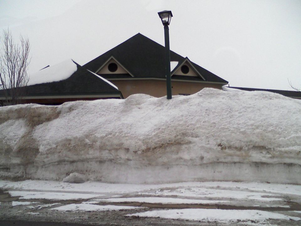 Huge snow pile in front of a building with a street lamp
