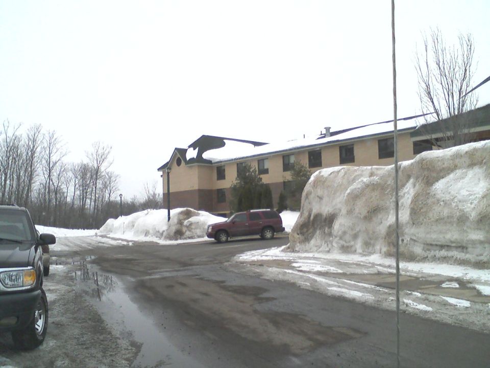 Maroon SUV parked on wet asphalt with snow piles, building in background