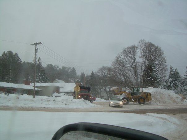 White car driving past snowplow and loader in snowy conditions