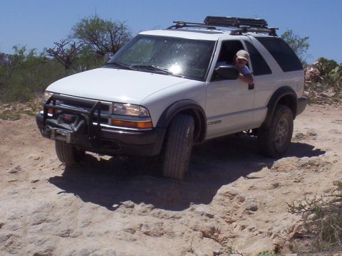 1992 Ford F-150 - A white SUV navigates a dusty, off-road trail under a clear blue sky.