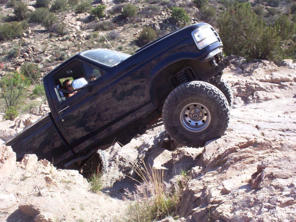 Lifted dark blue Ford F-150 pickup climbing a steep rock ledge on a desert trail