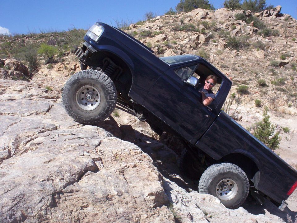 Dark Ford F-150 pickup climbing steep rocks at steep angle on large off-road tires
