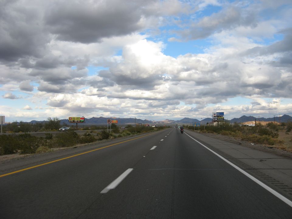 Motorcycle on a highway with a cloudy sky and desert landscape