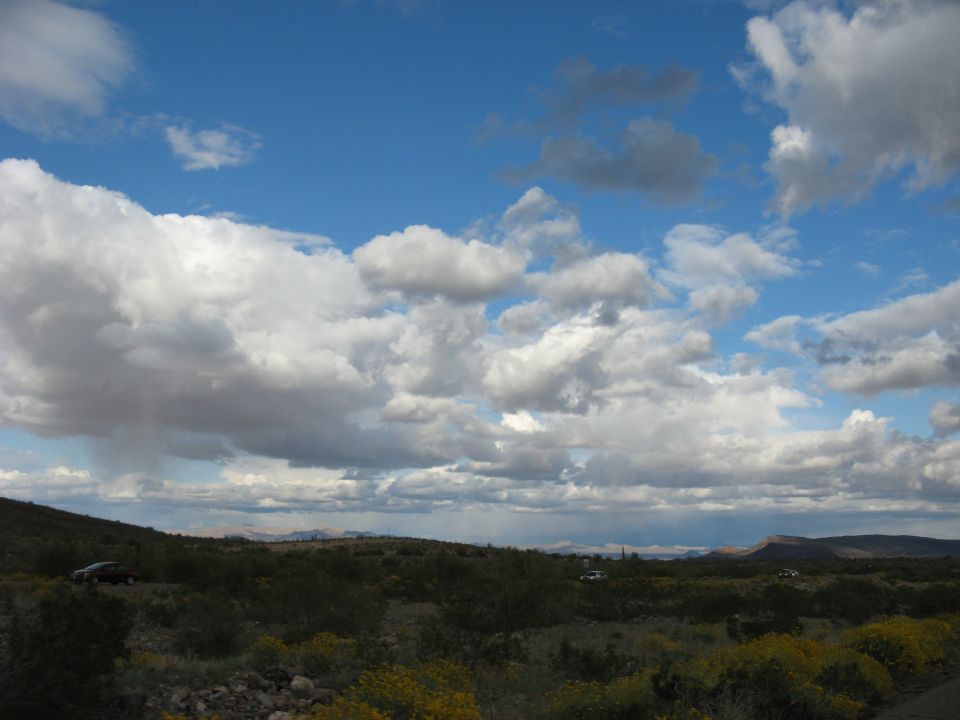 Several cars parked in a dry, brushy landscape under a cloudy sky