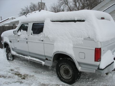 1995 Ford C-350 (Centurion Conversions) - A white pickup truck with a camper shell is parked outside, covered in a thick layer of snow.
