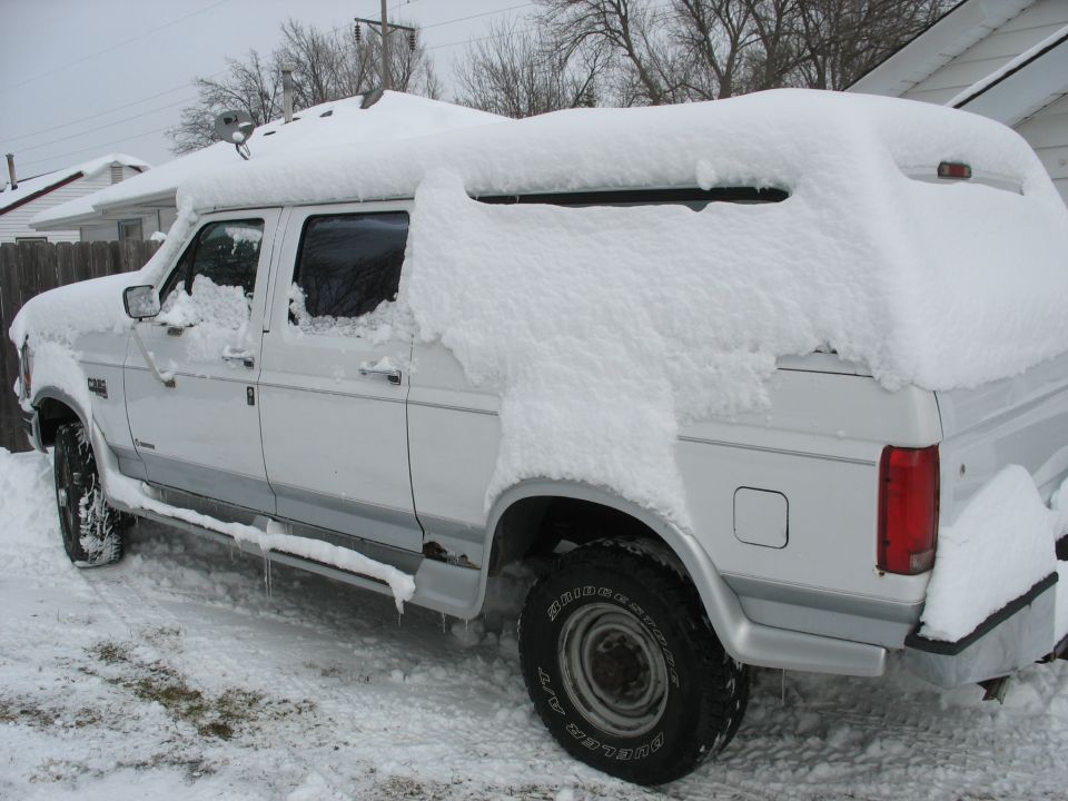 White extended cab pickup truck covered in snow, with a camper shell on the back