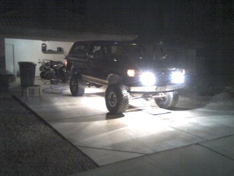 1991 Ford Bronco - A black Ford Bronco is parked in a garage with its headlights on.