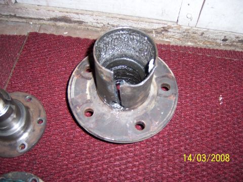 1991 Ford Bronco - A damaged wheel hub assembly sits on a red carpeted surface, showing a split metal sleeve.