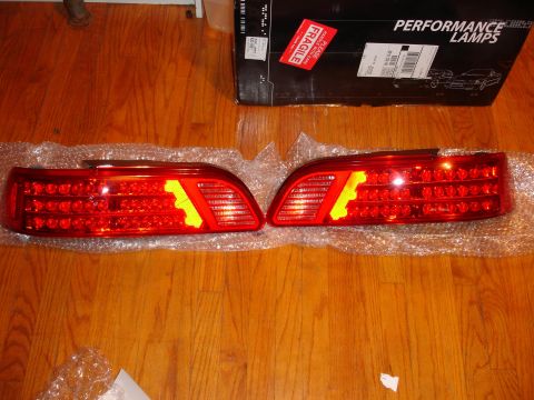 1993 Ford Taurus - A pair of aftermarket LED tail lights are displayed on a wooden surface, with a box for performance lamps in the background.