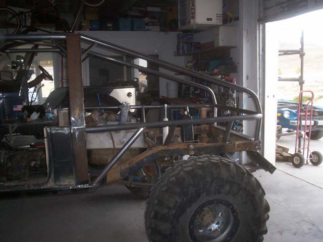 Vehicle chassis with custom roll cage being fabricated, large tire visible