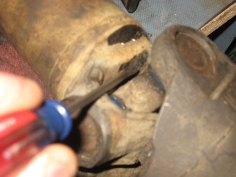 1990 Ford F-250 - A driveshaft U-joint is worked on with a screwdriver, showing a close-up of the mechanical component.